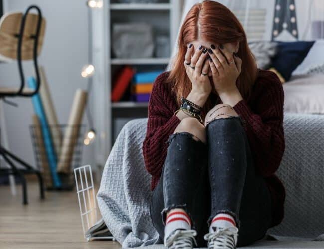 Teenage girl sitting on the floor and crying because of problems at home with parents